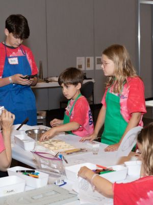 5 kids wearing aprons around a table with jewelry maker teacher during FutureFusion at AJS