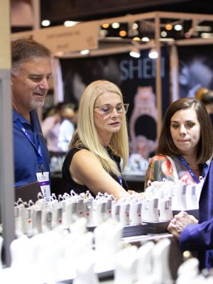 A group of people looking at the jewelry displayed at a busy trade show booth.